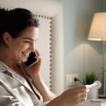 woman-in-cozy-bedroom-smiling-while-holding-pregnancy-test-and-talking-on-phone-showcasing-joyful-moment-of-anticipation-and-excitement-for-future-family-photo